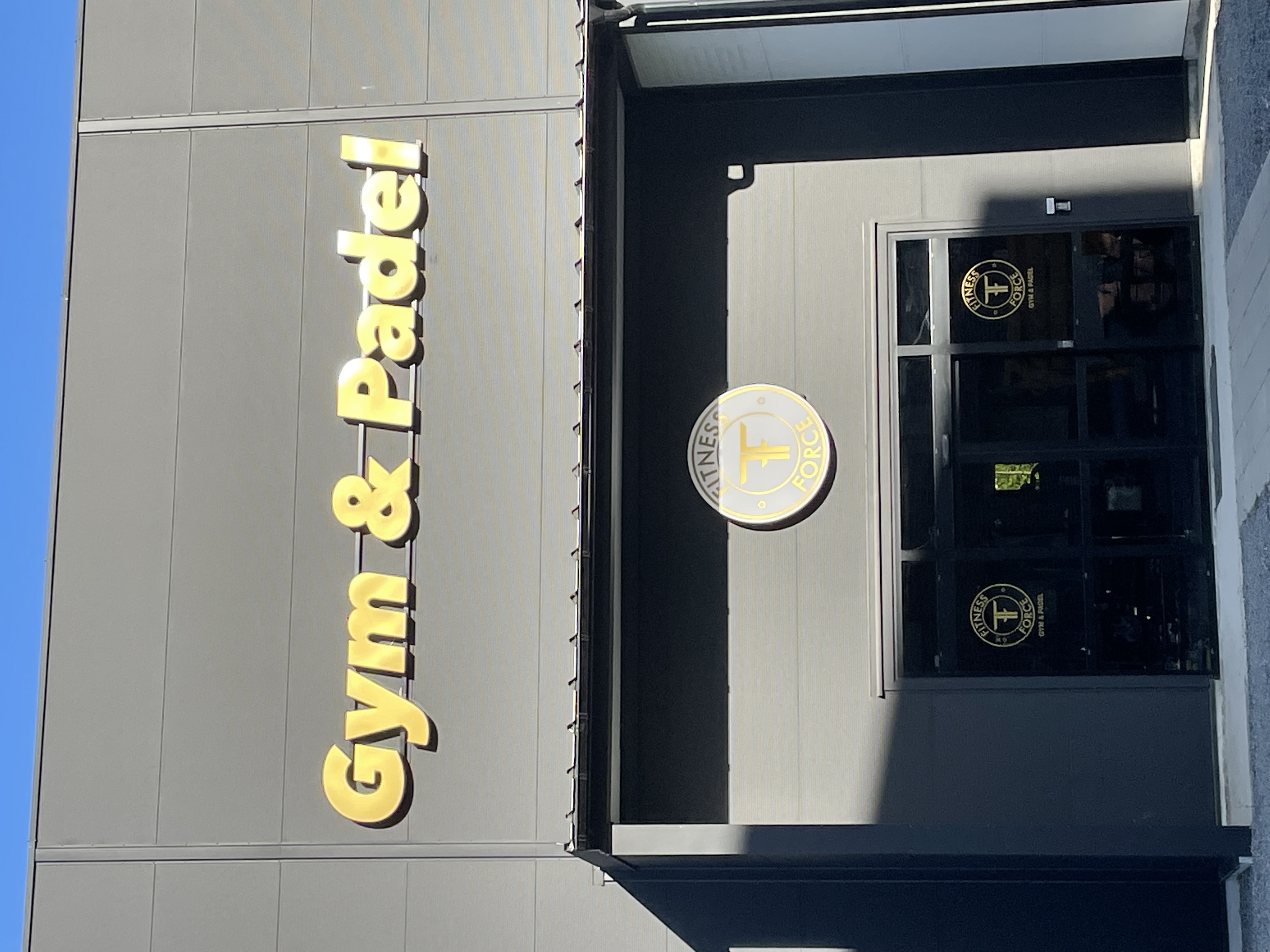Gym & Padel-skylt i guld ovanför entrén